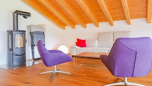 A modern living room with a wooden ceiling, a fireplace, two purple chairs, a white sofa, and a red pillow. - Kronenplatz 11 OG by Interhome (Lenk)