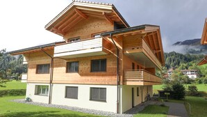 A two-story wooden house with a balcony, surrounded by a green landscape and mountains in the background. - Kronenplatz 11 OG by Interhome (Lenk)