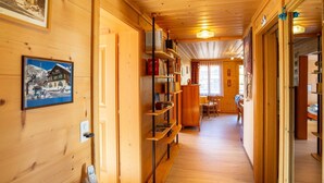 A wooden interior with a long hallway, a bookshelf, a dining area, and a door leading to another room. - Berna 2. Stock by Interhome (Lenk)