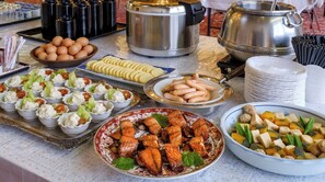 Une table de buffet proposant divers aliments, notamment des œufs, des tranches de pain, des saucisses et un plat de saumon grillé.