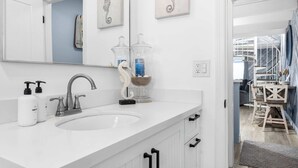 A modern bathroom with a white sink, a mirror, and a seahorse artwork.