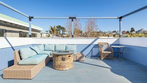 A rooftop patio with a wicker sofa, a round stone table, and wicker chairs.