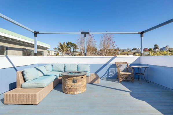 A rooftop patio with a wicker sofa, a round stone table, and wicker chairs.