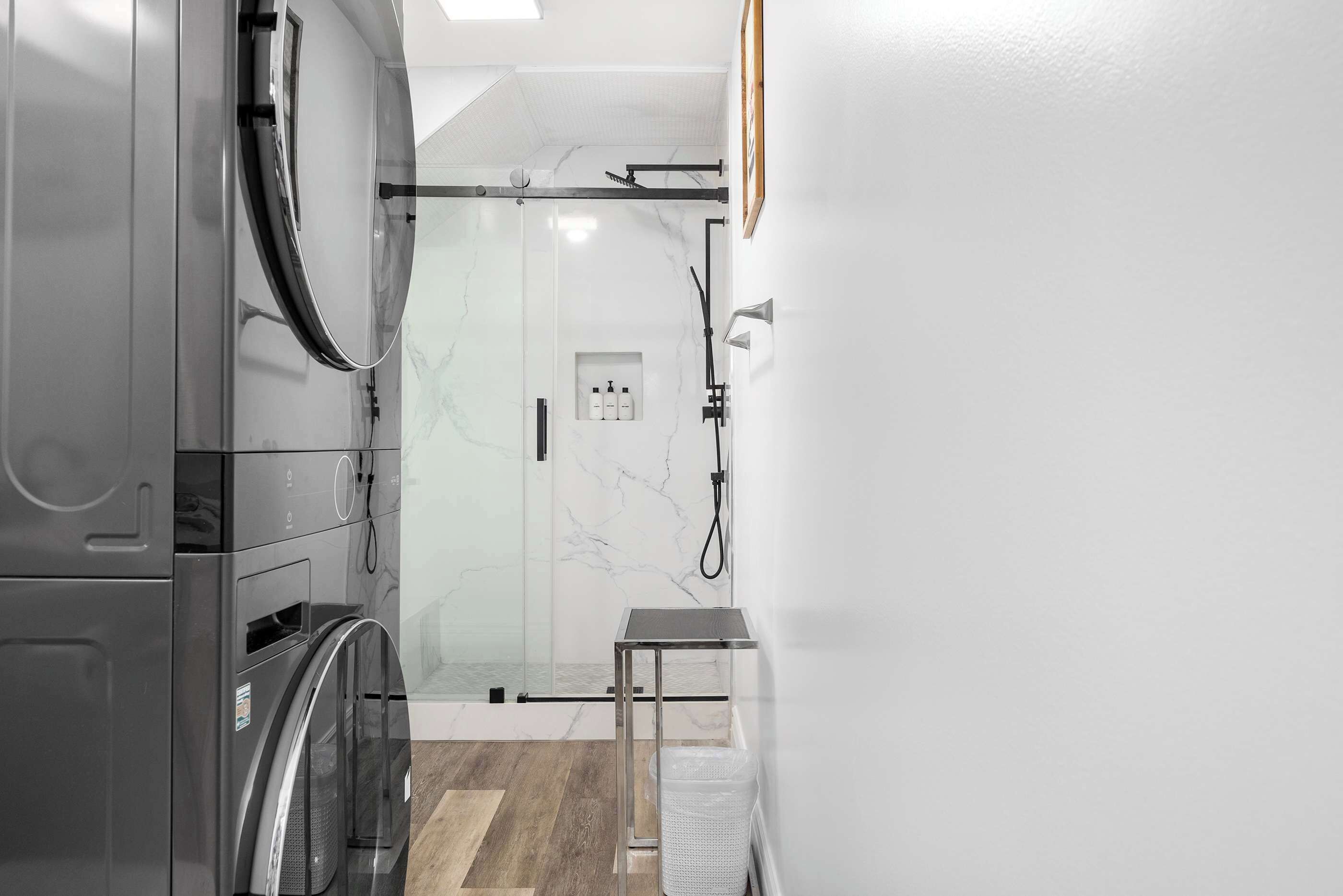 Un baño moderno con cabina de ducha de vidrio, lavadora integrada y una pequeña mesa.