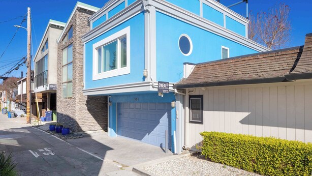 A two-story building with a blue facade, a garage door, and a small garden area.