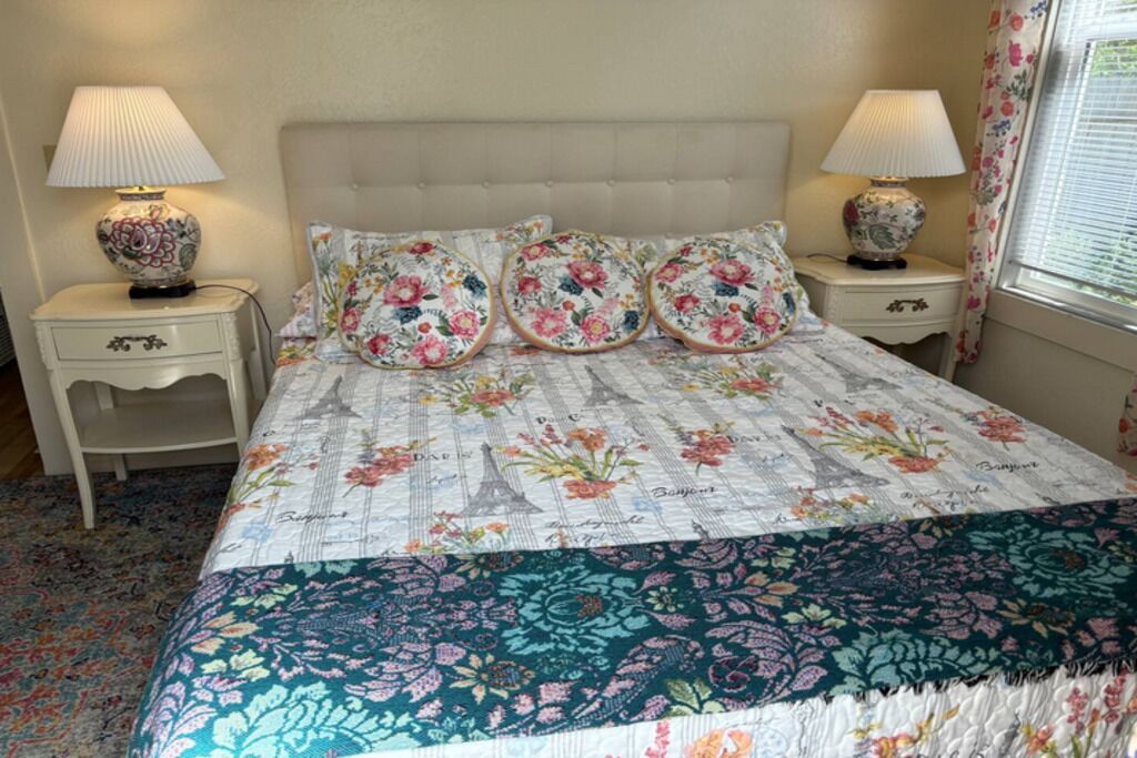 A bedroom with a floral bedspread, two bedside lamps, and a window with curtains.