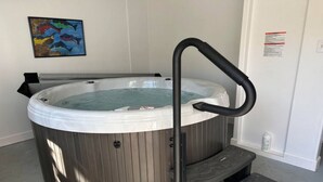 Una vasca idromassaggio con rivestimento in legno, una scaletta in metallo nero e un piccolo gradino per accedervi.