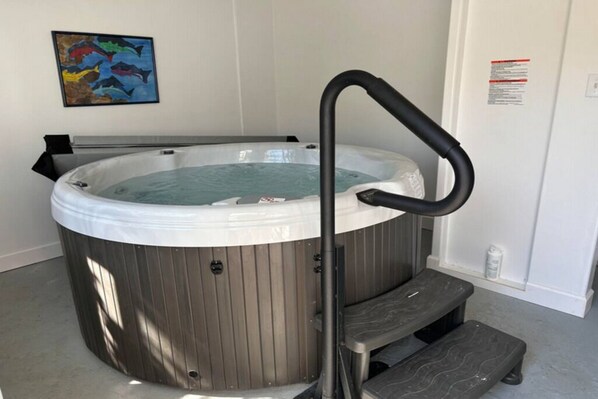 A hot tub with a wooden exterior, a black metal ladder, and a small step for access.