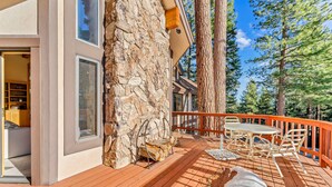 A wooden deck with outdoor furniture, a stone wall, and a view of trees.