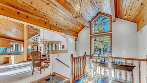 A spacious interior with a wooden ceiling, a dining area with a chandelier, and a view through a large window.