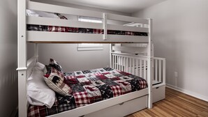 Una cama litera con colcha acolchada, una cuna blanca y suelo de madera.