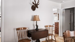 Un comedor con una mesa y sillas de madera, una lámpara y una cornamenta de ciervo en la pared.