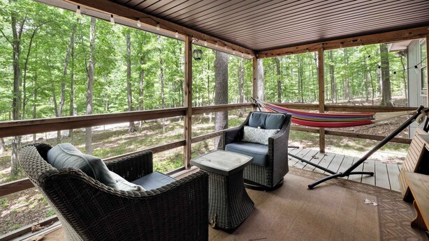 Un espacio al aire libre cubierto con mobiliario de mimbre, una hamaca y vistas a un bosque.