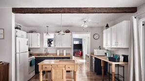 Una cocina moderna con armarios blancos, una mesa de comedor de madera, un ventilador de techo y un reloj en la pared.
