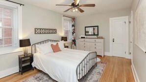 A bedroom with a bed, nightstand, dresser, ceiling fan, and a window with blinds. - Sojourn at Colley Manor Unit 4 (Norfolk)