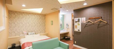 A hotel room with a bed, a green sofa, a glass table, a wall-mounted TV, and a wardrobe with a mirror.