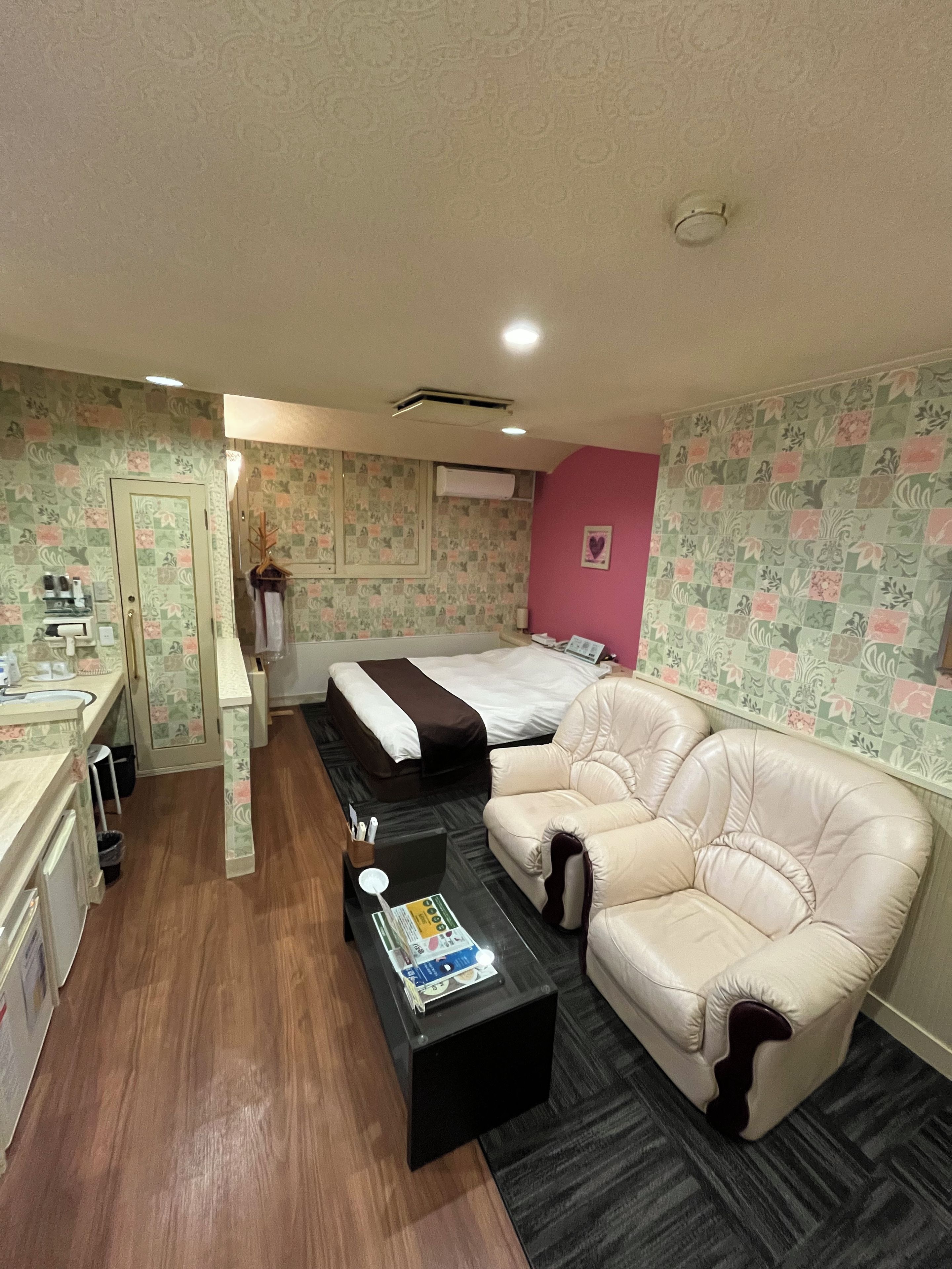 A compact hotel room with a bed, a sofa, a small table, and a kitchenette.