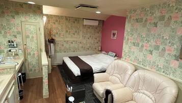 A compact hotel room with a bed, a sofa, a small table, and a kitchenette.