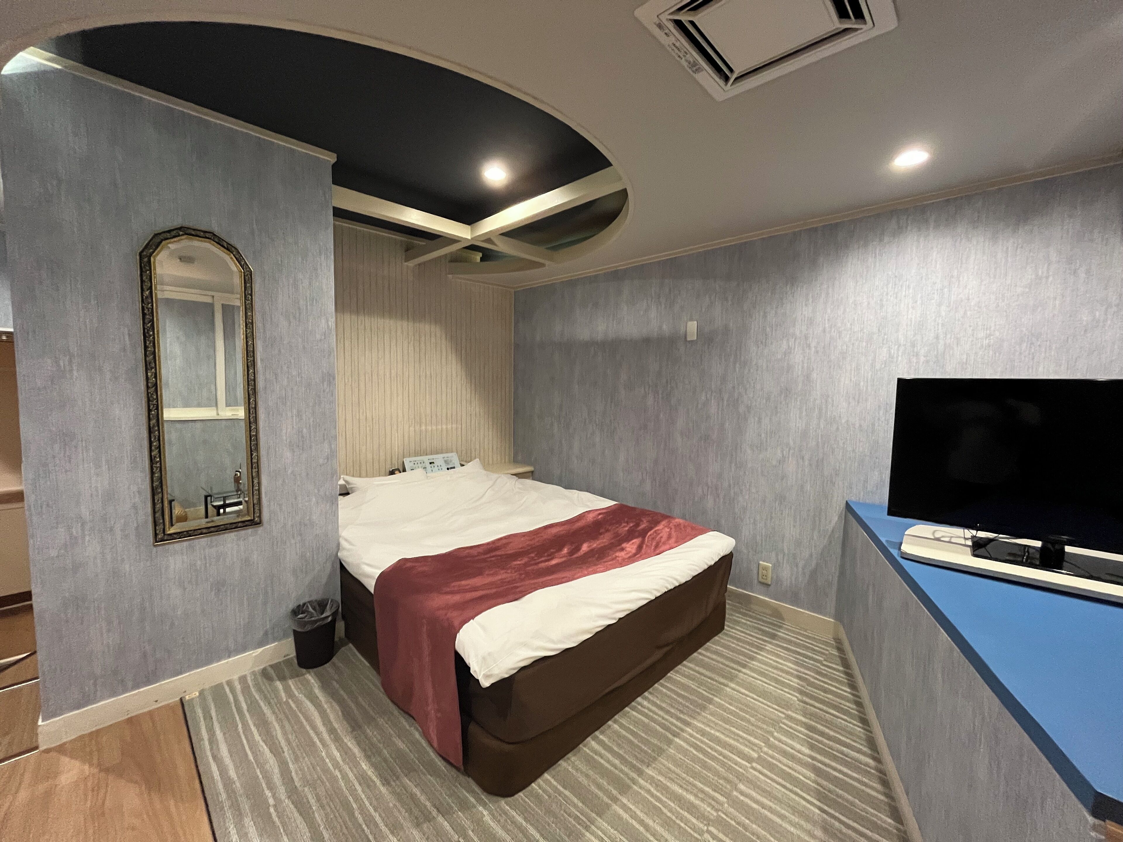 A hotel room with a bed, a TV, a mirror, and a small desk.