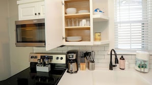 A kitchen with a microwave, stove, coffee maker, and a cabinet with dishes and utensils. - Sojourn at Colley Manor Steps from Local Favorites Unit #6 (Norfolk)