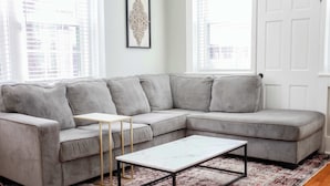 A gray sectional sofa with a white coffee table and a small side table, positioned on a patterned rug. - Sojourn at Colley Manor Steps from Local Favorites Unit #6 (Norfolk)
