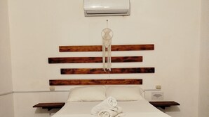 Une chambre à coucher avec une tête de lit en bois, un couvre-lit blanc, une table de chevet et un climatiseur fixé au mur.