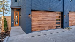 Una casa moderna de dos pisos con puerta de garaje, puerta principal de madera y un pequeño jardín.
