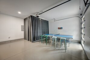 A room with a ping pong table, two stools, a projector, and a curtain.