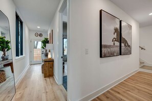 A modern hallway with wooden flooring, a mirror, and two framed pictures on the wall.