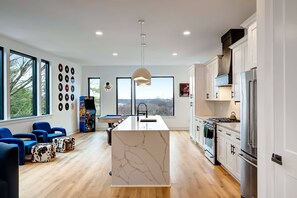 A modern kitchen with a central island, white cabinetry, and a large window offering a view of the outdoors.