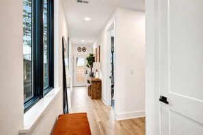 A modern hallway with a wooden floor, a bench, and a view of the outdoors through large windows.