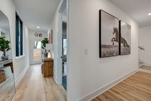 A modern hallway with wooden flooring, a mirror, a wooden bench, and two framed pictures on the wall. - Rooftop hot tub, sauna & game room house near Geodis Park, sleeps 12 (Nashville)