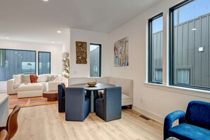 A modern living room with a round table, blue chairs, a white sofa, and artwork on the walls.