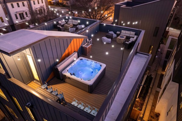 A rooftop deck with a hot tub, outdoor seating, and string lights.
