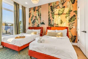 A hotel room with two beds, a large window, and a tropical leaf-patterned wall.