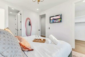 A modern hotel room with a large bed, a TV mounted on the wall, and a wooden tray with bottles and a candle.