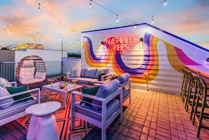 An outdoor seating area with a colorful mural and string lights. - Nashville-themed rooftop bar retreat, sleeps 12 near Geodis Park (Nashville)