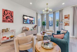A modern living room with a sofa, chairs, a coffee table, and a TV mounted on the wall. - Fall in Nashville: themed house with garage game room near Geodis Park (Nashville)