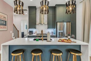 Una cocina moderna con una isla central, taburetes de bar, electrodomésticos de acero inoxidable e iluminación colgante.