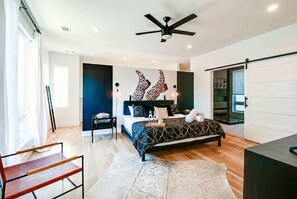 Un dormitorio moderno con cama, escritorio, silla, ventilador de techo y vistas al exterior.