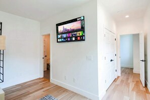 Un moderno salón con un televisor de pantalla plana montado que muestra varias aplicaciones de streaming, paredes de color claro y suelo de madera.