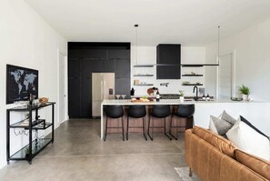 A modern kitchen with a central island, bar stools, and a black-framed TV on the left. - Fall getaway: 2 homes, rooftop decks, sleeps 20 near The Gulch (Nashville)