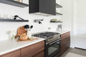 A modern kitchen with a gas stove, oven, wooden cabinets, and a white countertop.