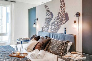 Une chambre d’hôtel moderne avec un grand lit, une table de chevet, une lampe fixée au mur et une fenêtre avec des rideaux.