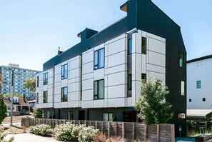 A modern multi-story building with a flat roof, large windows, and a wooden fence surrounding the property. - Nashville getaway: 2 rooftop homes, sleeps 20, 6 bedrooms in the Gulch (Nashville)