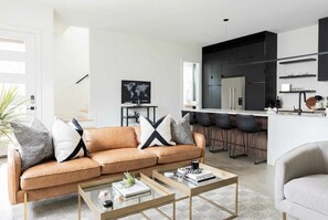 Una sala de estar moderna con sofá, una mesa de centro y una zona de cocina con taburetes de bar.