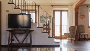 A modern living room with a flat-screen TV on a wooden stand, a staircase with metal railings, and two upholstered chairs.