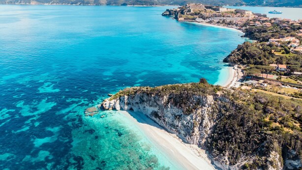 A coastal town with a beach, clear blue waters, and a mountainous backdrop.