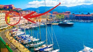 A marina with boats docked, a waterfront promenade, and colorful buildings in the background.