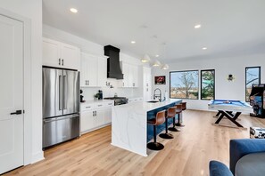 A modern kitchen with white cabinets, stainless steel appliances, and a marble island. - Nashville house with hot tub & pool table, sleeps 12 near Geodis Park (Nashville)
